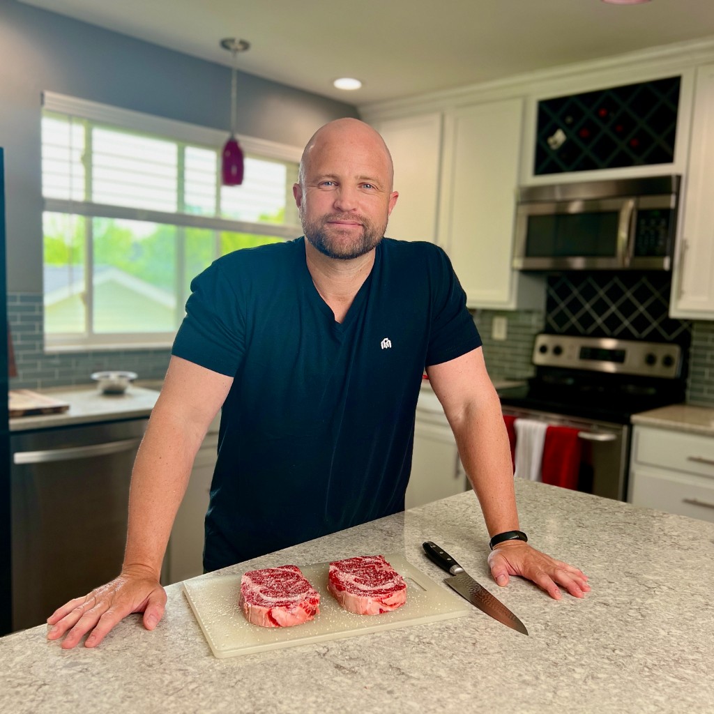 Joe Lampe in his kitchen with seasoned ribeye steaks and a chef knife for the Red Meat Lover cooking brand